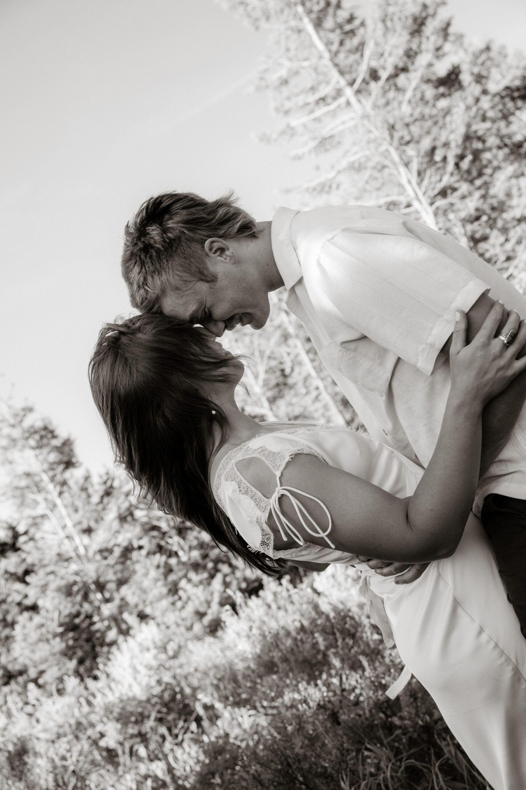 Engaged couple snuggled by a mountain lake in cozy neutral outfits for a fall destination engagement session